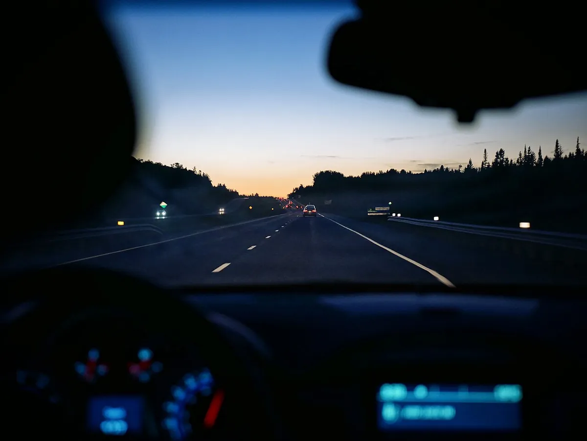 Vue depuis la place du conducteur sur une route au crépuscule, tableau de bord allumé